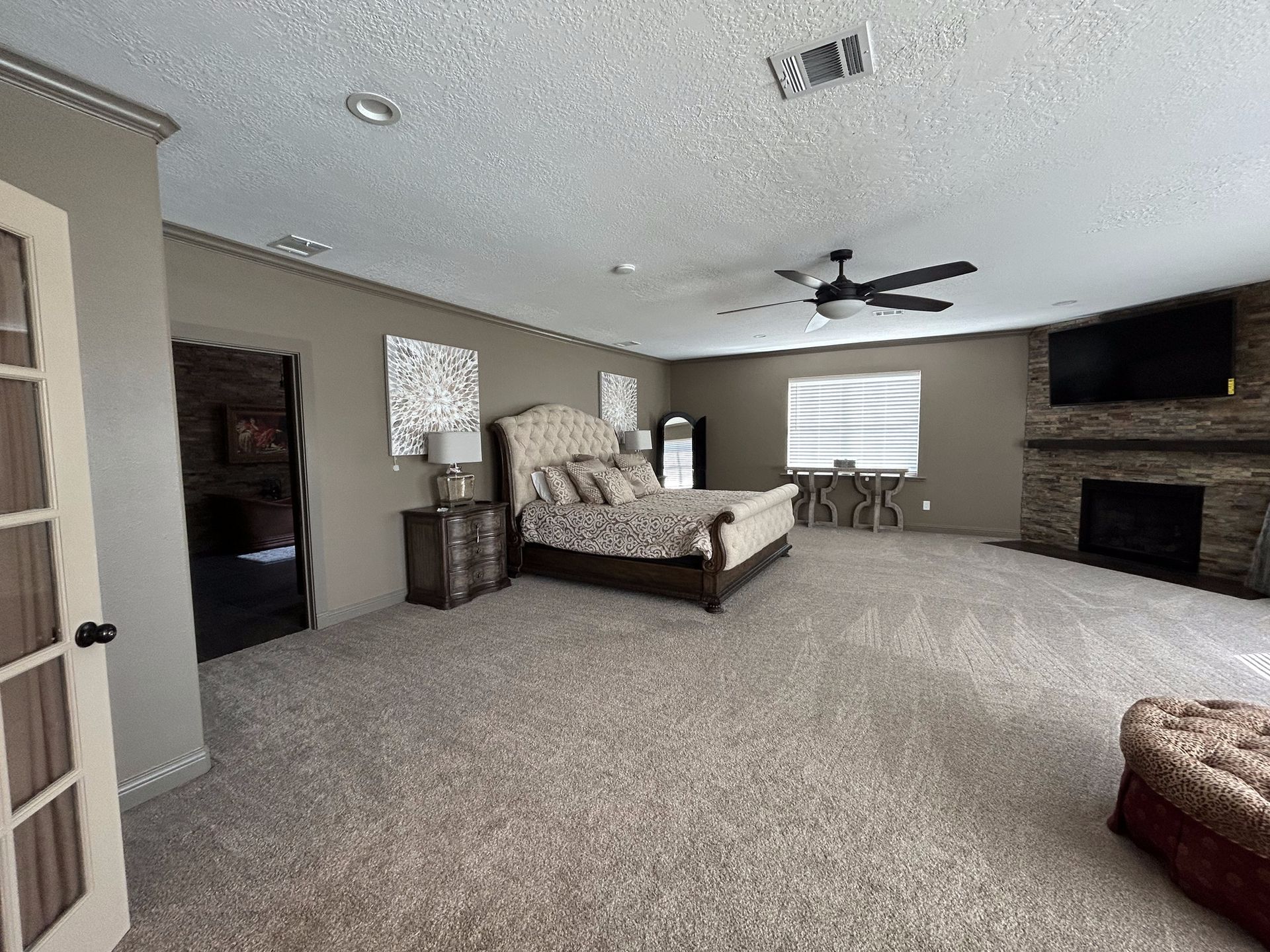 A large bedroom with a bed , fireplace , television and ceiling fan.