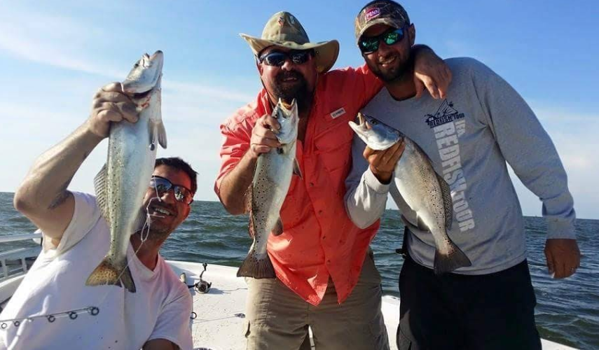 Three men are standing on a boat holding fish.