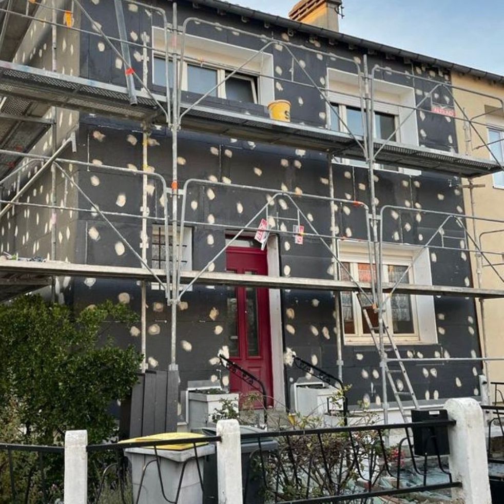 Une maison avec un échafaudage autour et une porte rouge.