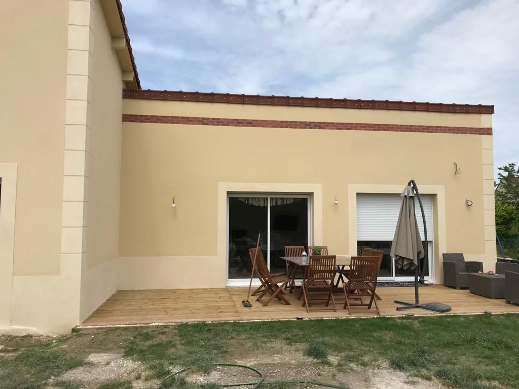 Une maison avec un patio avec une table, des chaises et un parasol