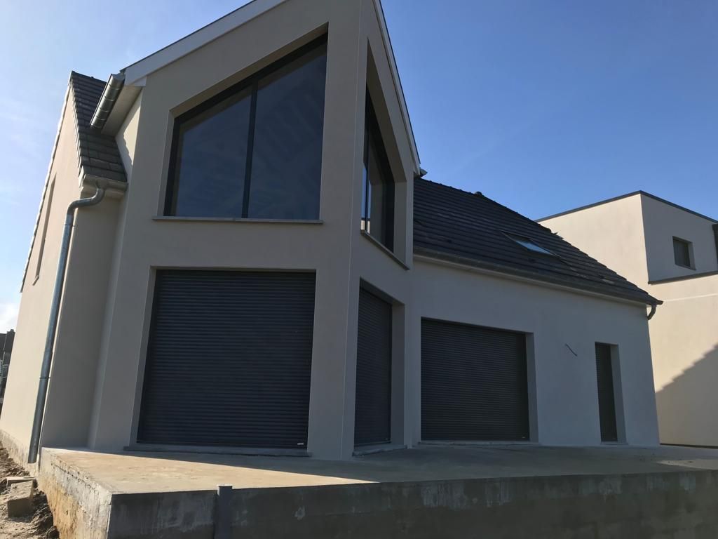 Une maison blanche avec une porte de garage noire et un ciel bleu en arrière-plan