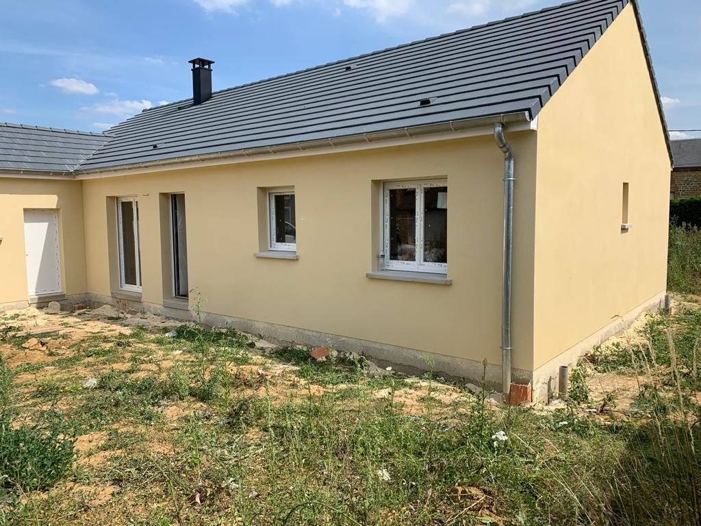 Une maison jaune avec un toit gris et des fenêtres blanches