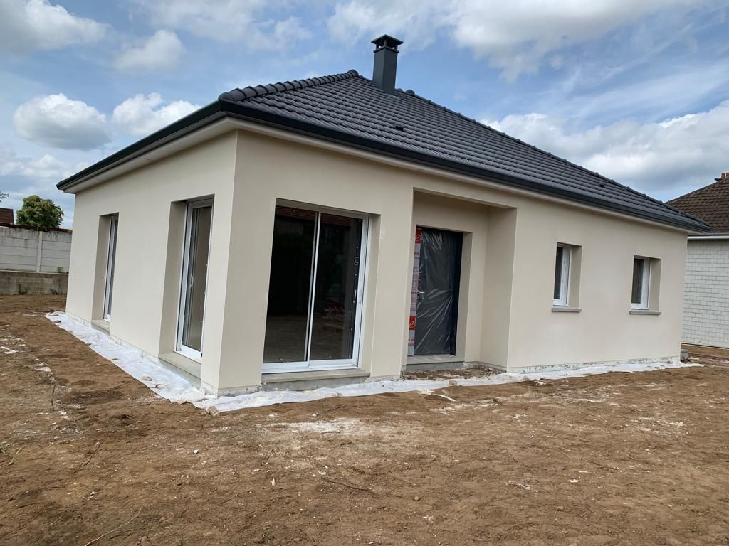 Une maison blanche avec un toit noir se trouve au milieu d'un champ de terre.