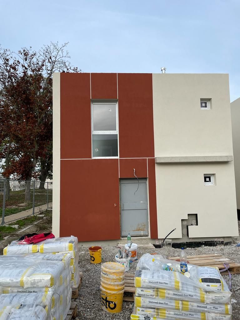 Une maison est en train d'être construite avec des seaux et des sacs de ciment devant elle.