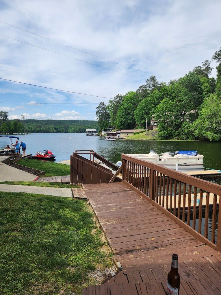 A bottle of beer is sitting on a wooden deck overlooking a lake.