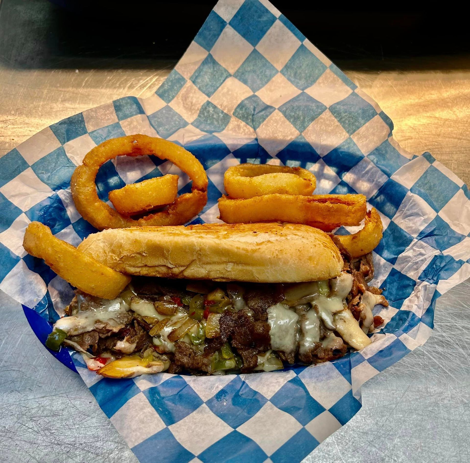 A sandwich and onion rings on a blue and white checkered paper