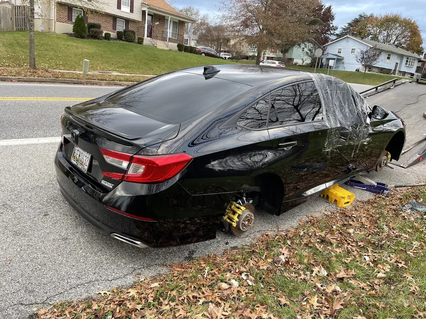 Black car on the side of a road; tires stolen, car is jacked up on yellow blocks.