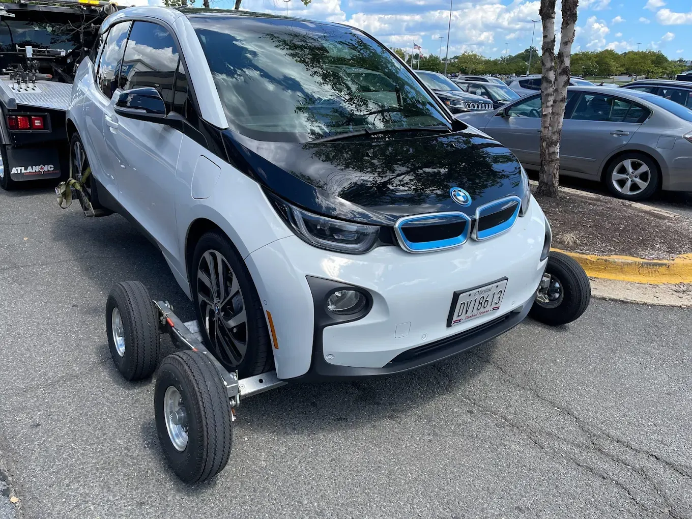 White BMW i3 electric car being towed with its front wheels on a dolly in a parking lot.