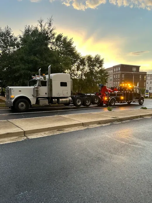 White semi-truck being towed by a tow truck on a wet road at sunset.