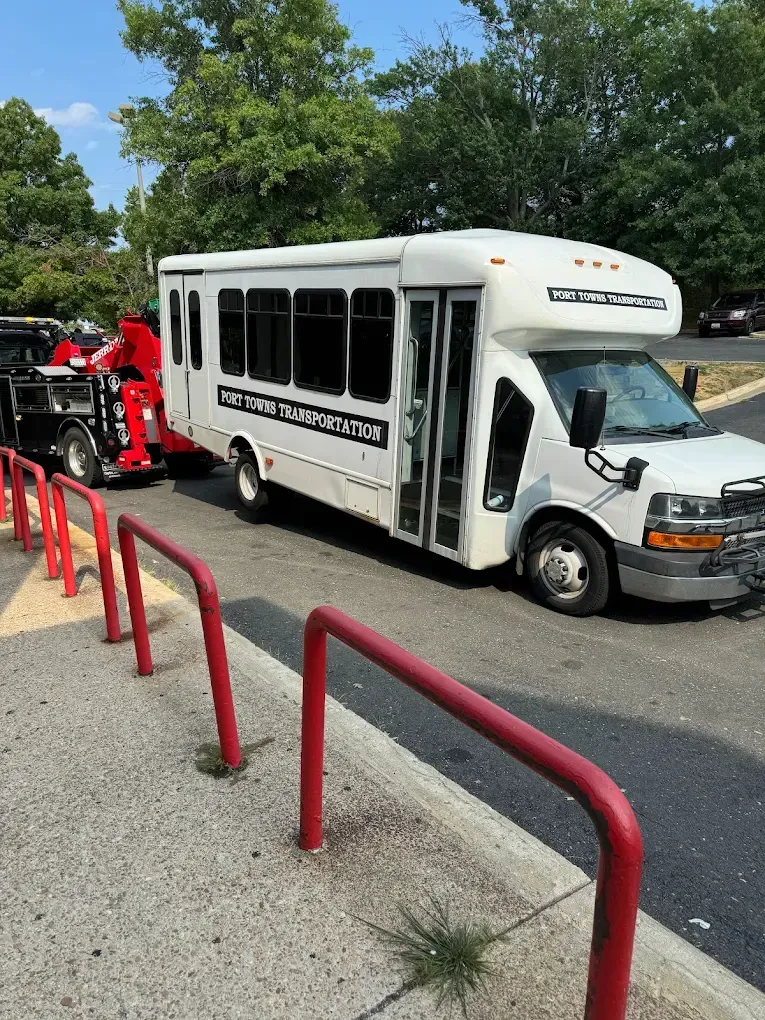 White bus with black windows next to red barrier. Another vehicle with red attire is attached.