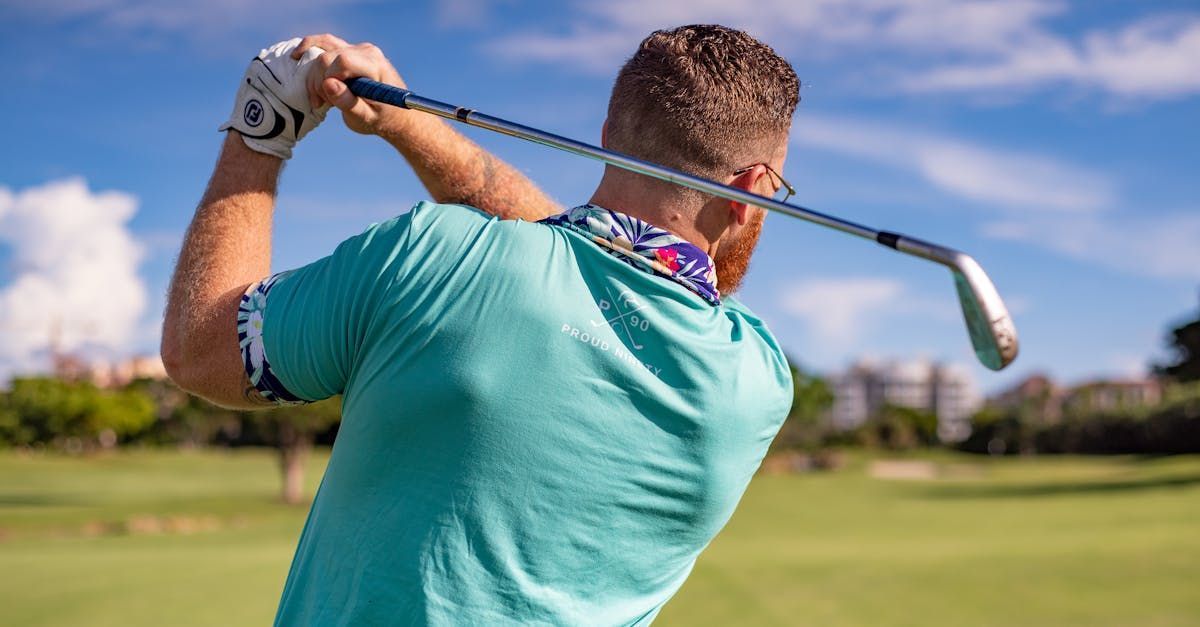 Golfer in turquoise shirt swinging a club on a green golf course.