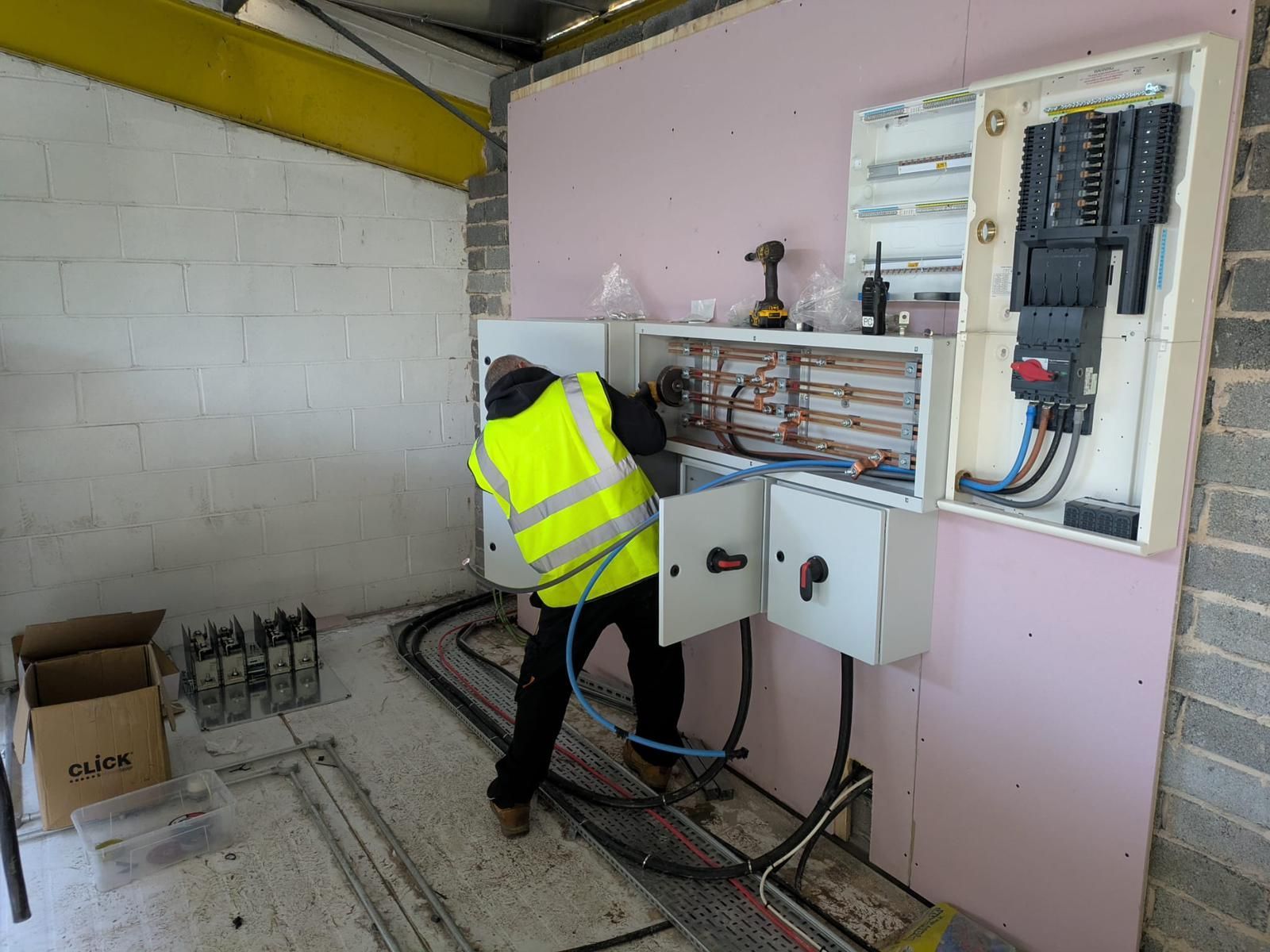 Electrician in a yellow vest working on electrical panel installation in a construction setting.
