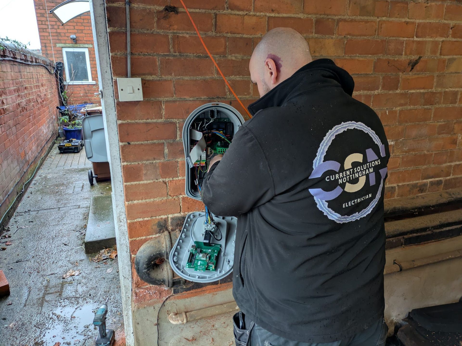 Electrician working on a gray electrical box mounted on a brick wall. The box is open, revealing wires.