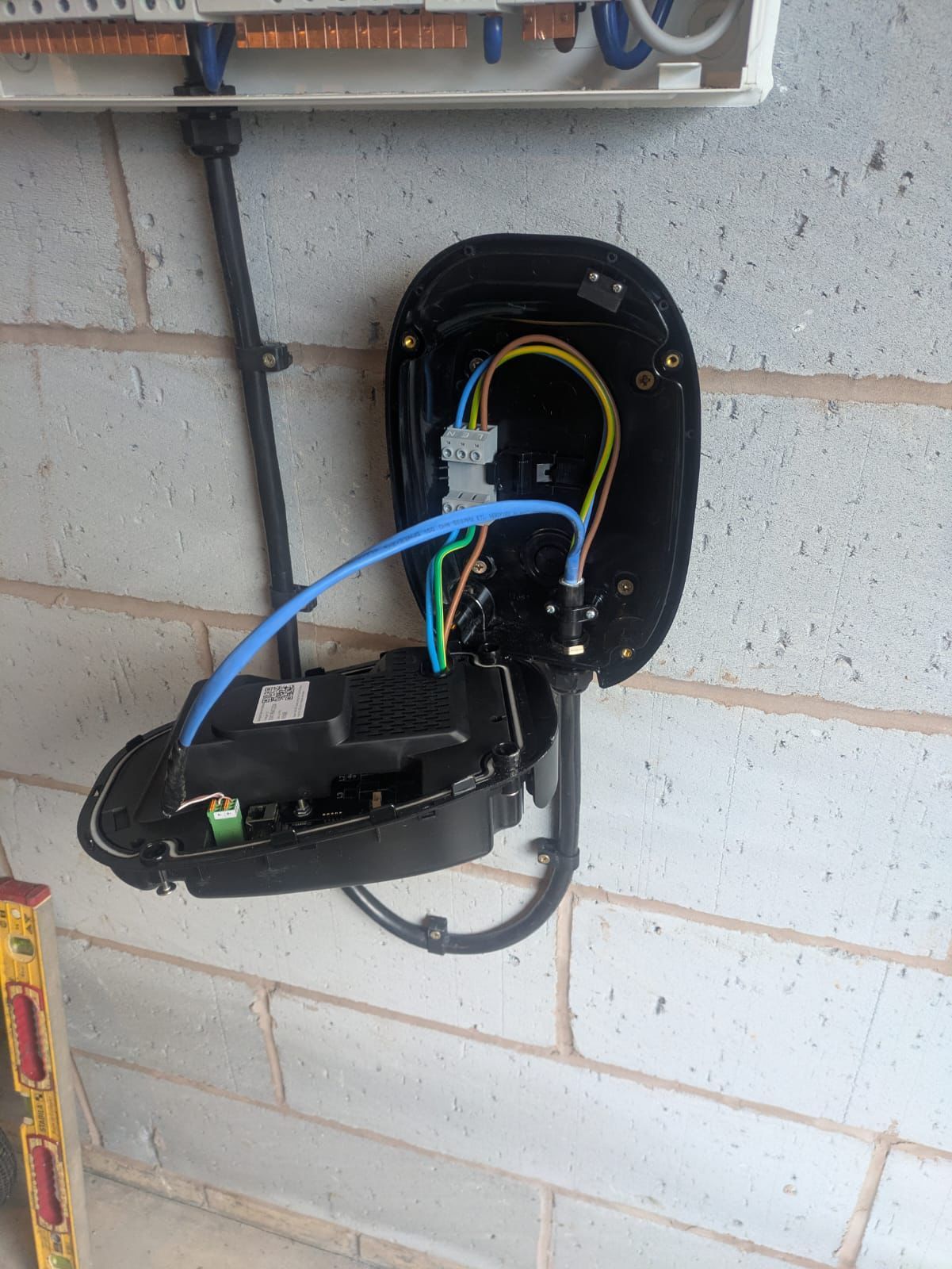 EV charger with open casing exposing wires, mounted on a brick wall.