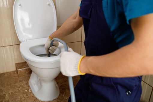 Person wearing gloves using a plumbing snake to unclog a toilet.