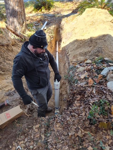 Man in a trench installing PVC pipe outdoors.