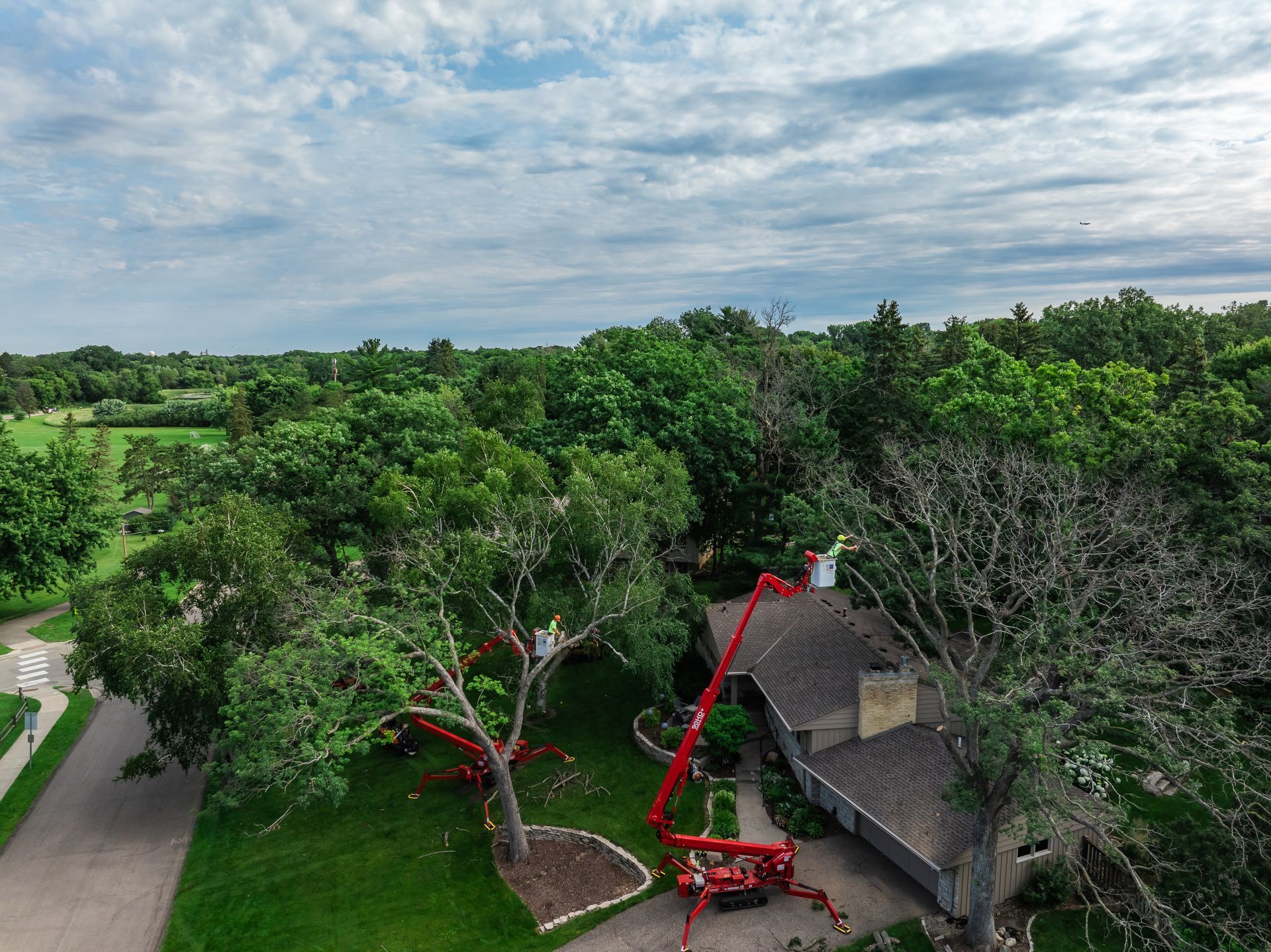 An aerial view of a tree being cut down by a crane in front of a house.