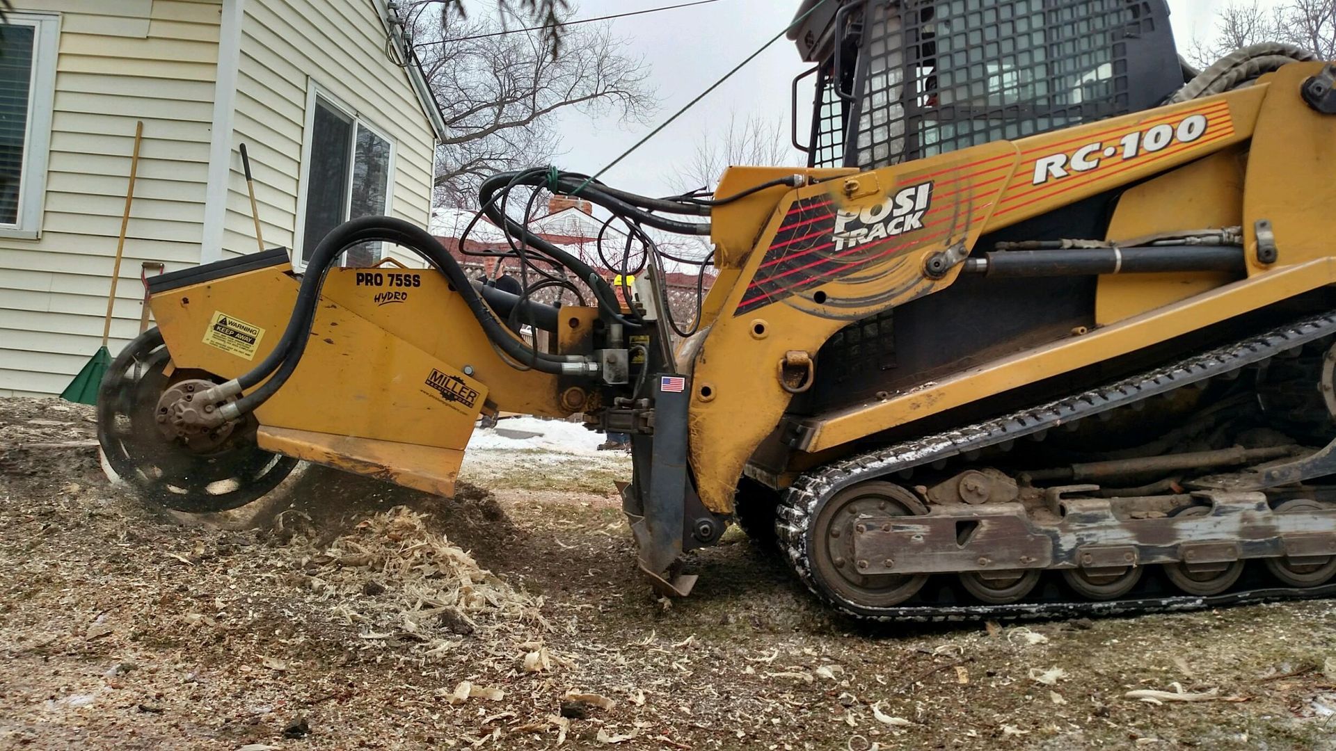 A yellow tractor is sitting in the dirt in front of a house.