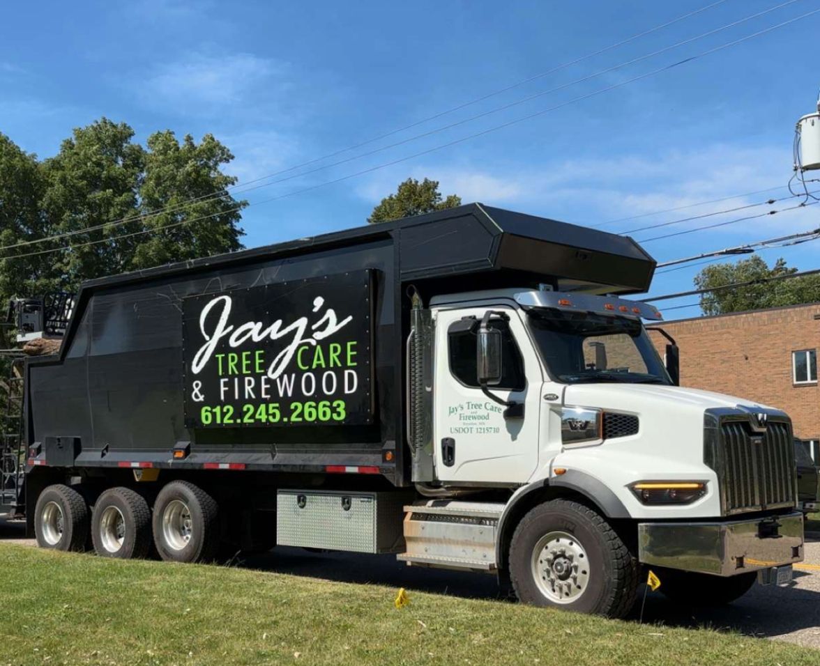 A dump truck for jay 's tree care and firewood is parked on the side of the road.