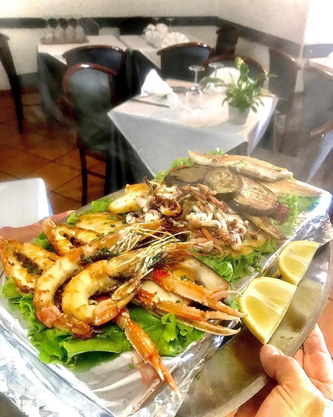 Un piatto di frutti di mare misti grigliati, servito su un letto di lattuga con spicchi di limone, in un ambiente da ristorante.