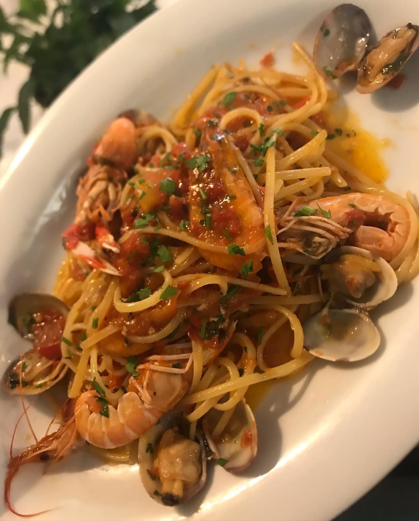 Un piatto di linguine condite con gamberi, vongole e una salsa a base di pomodoro, guarnite con erbe aromatiche fresche.