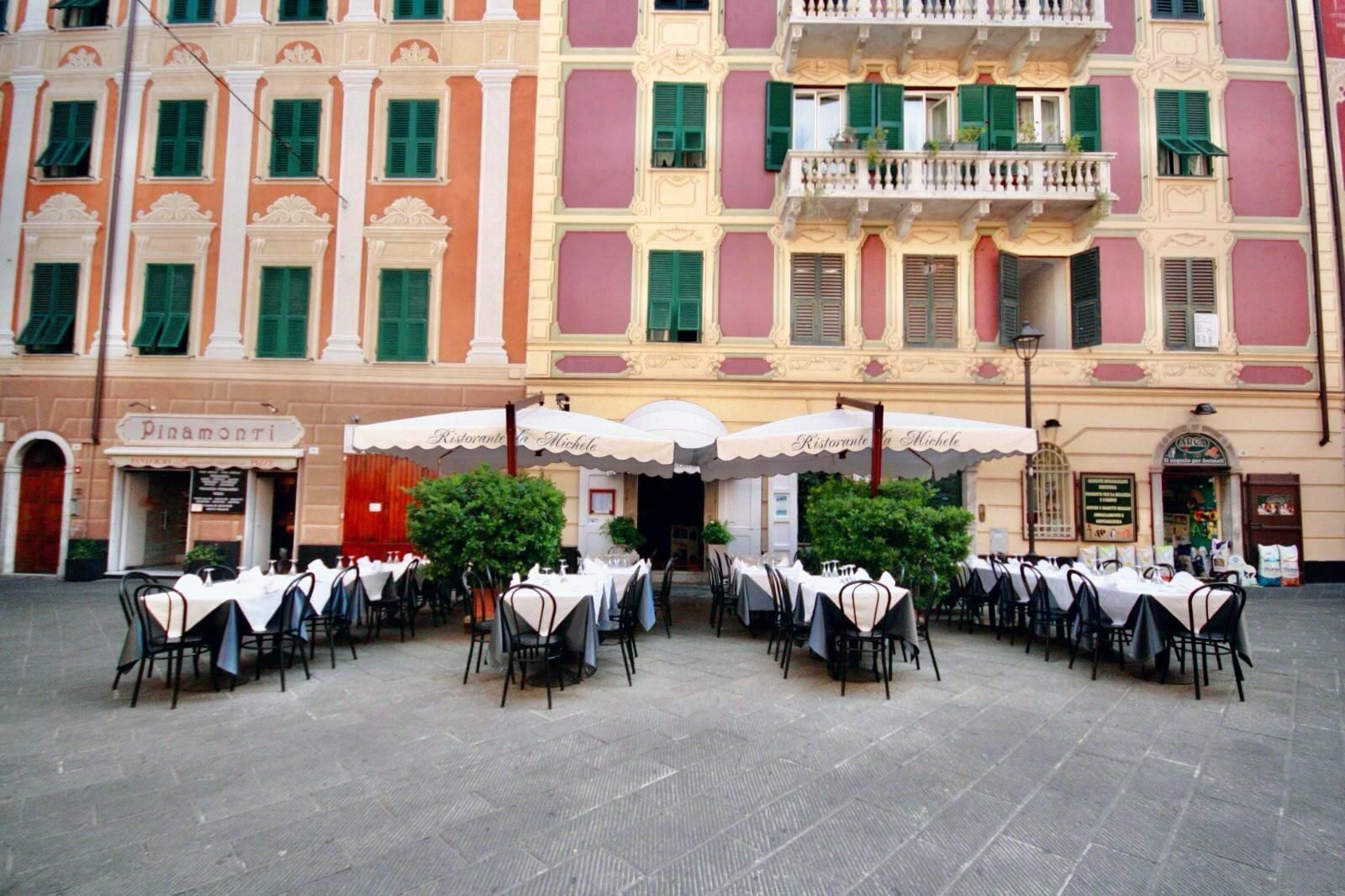Tavolini e sedie all'aperto in un caffè situato in una piazza storica con colorati edifici in stile mediterraneo.