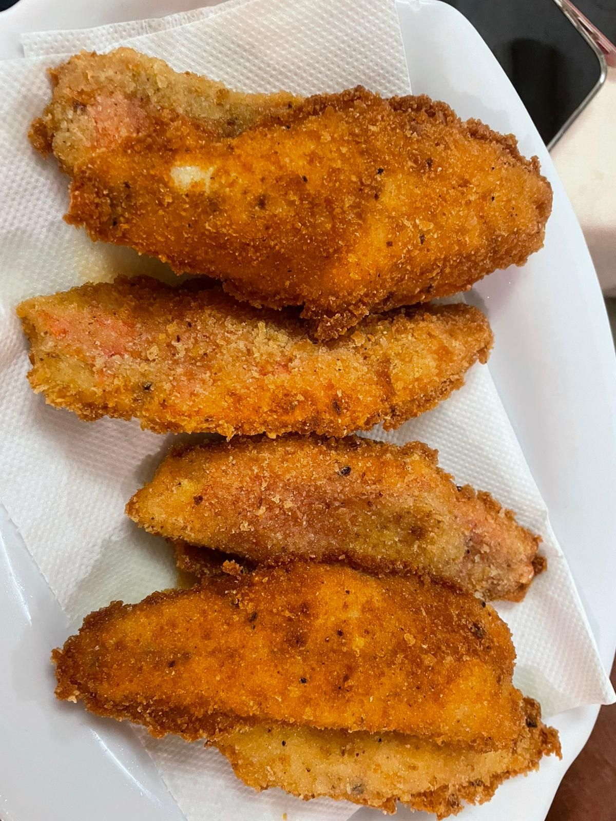 Quattro straccetti di pollo impanati e dorati, adagiati su un piatto bianco foderato con carta assorbente.