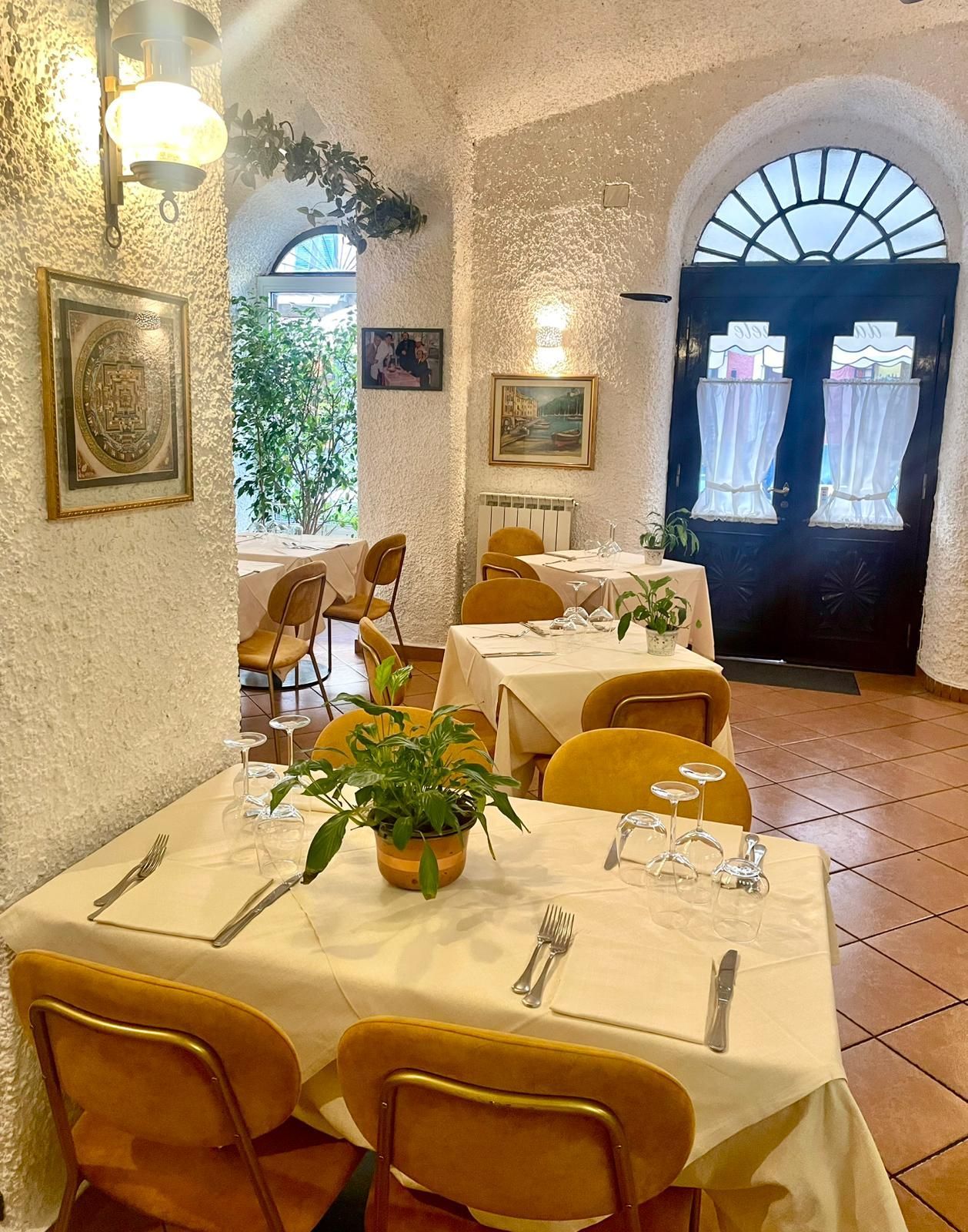 Vista interna di un'accogliente sala da pranzo di un ristorante con sedie gialle, tavoli apparecchiati, tovaglie bianche e porte ad arco.