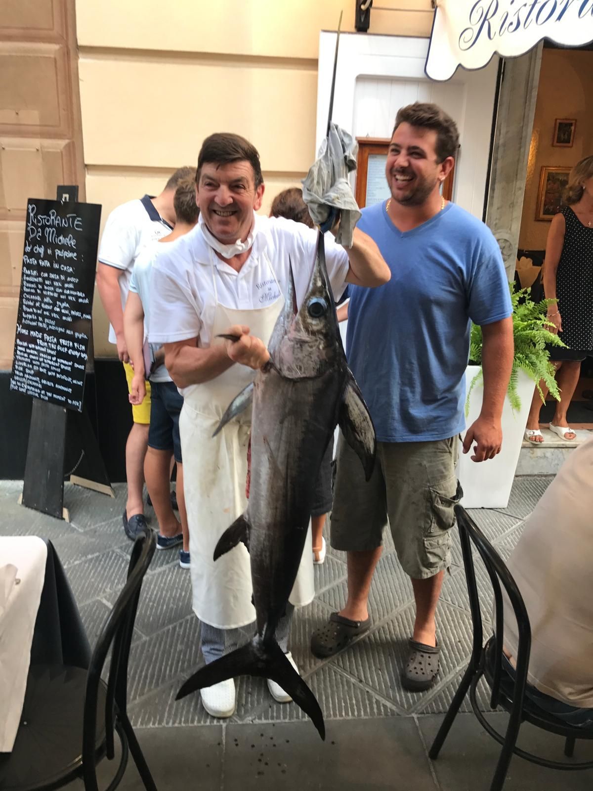 Uno chef e un uomo sono in piedi fuori da un ristorante, tenendo un grosso pesce per la coda.