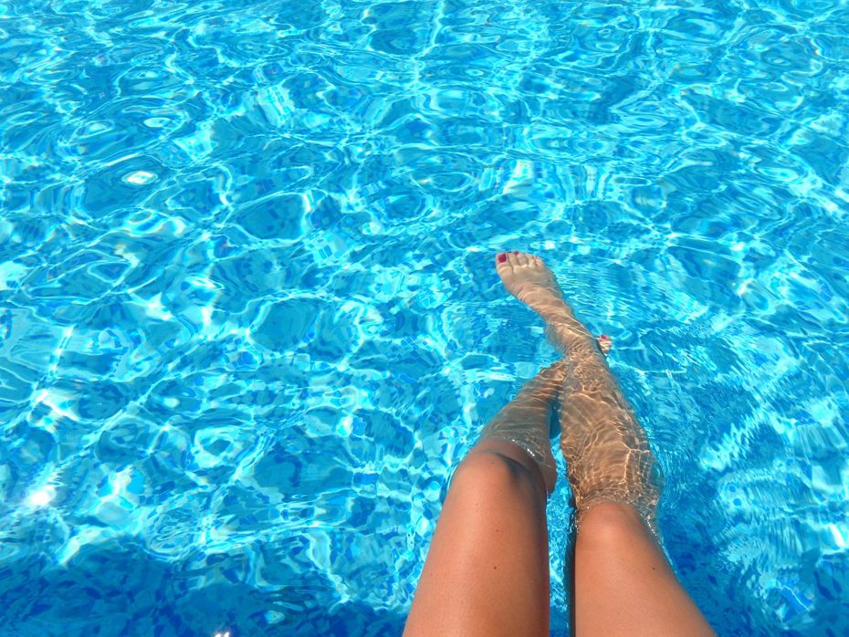 Legs resting in a bright blue swimming pool, with one foot crossed over the other.