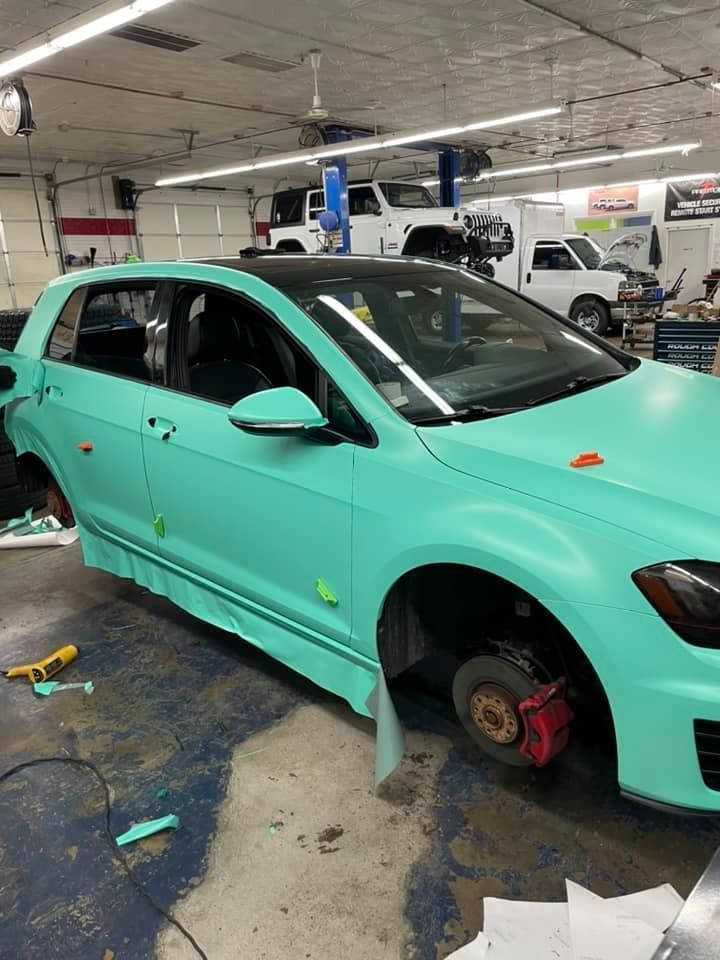 Mint-green sedan in a workshop with wheels removed, surrounded by tools and repair equipment