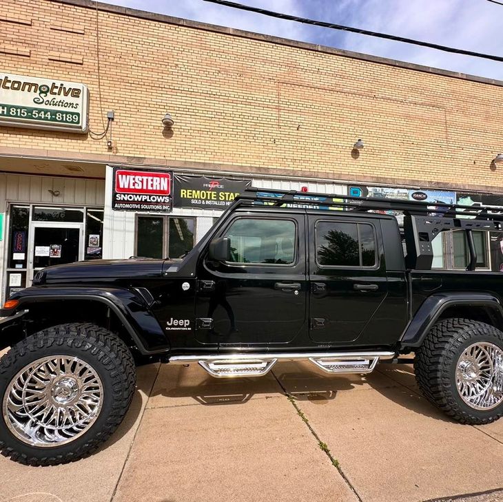 Black Jeep Wrangler parked outside a storefront on a sunny street
