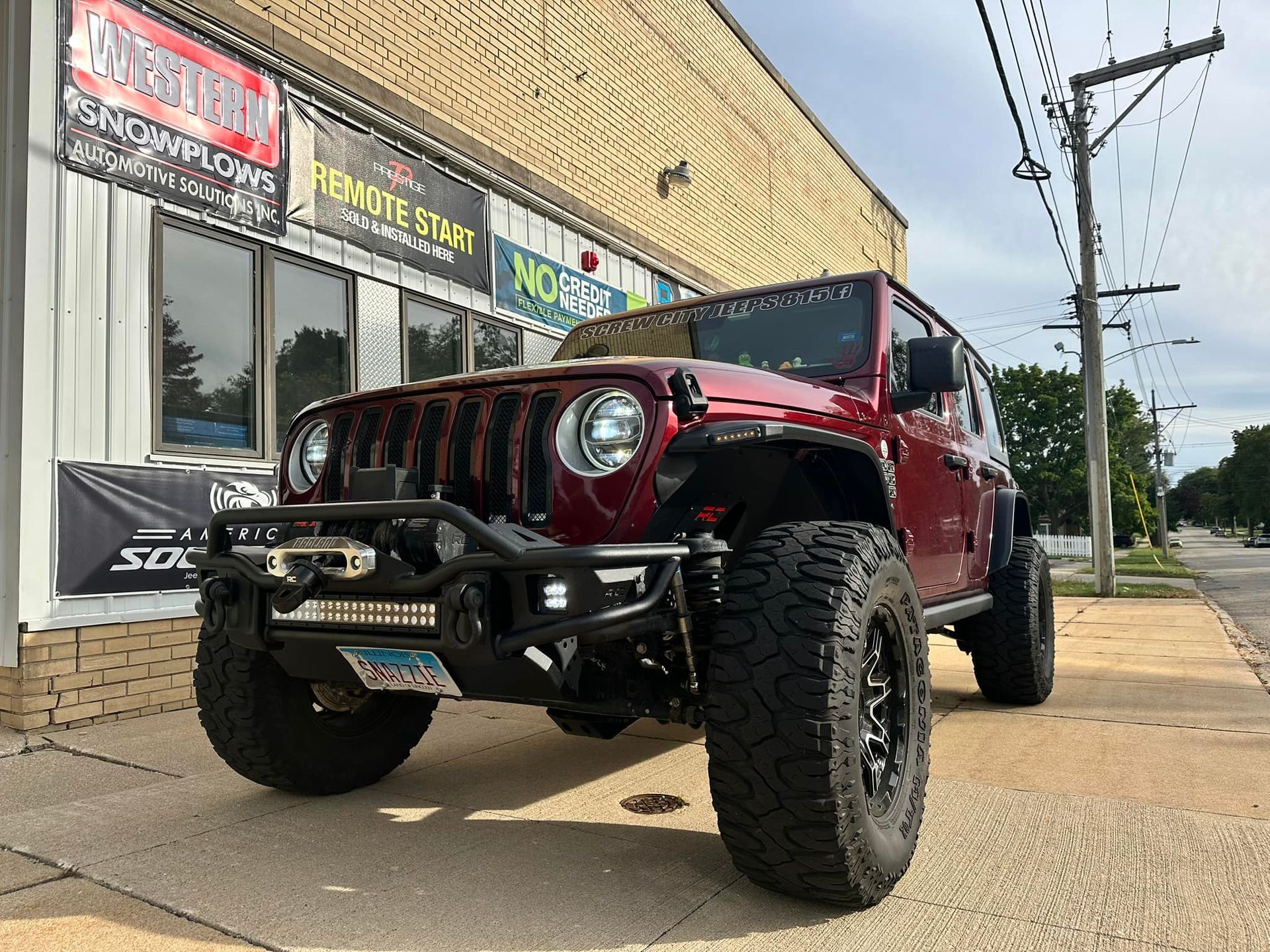 Red Jeep Wrangler parked outside a storefront on a sunny street.
