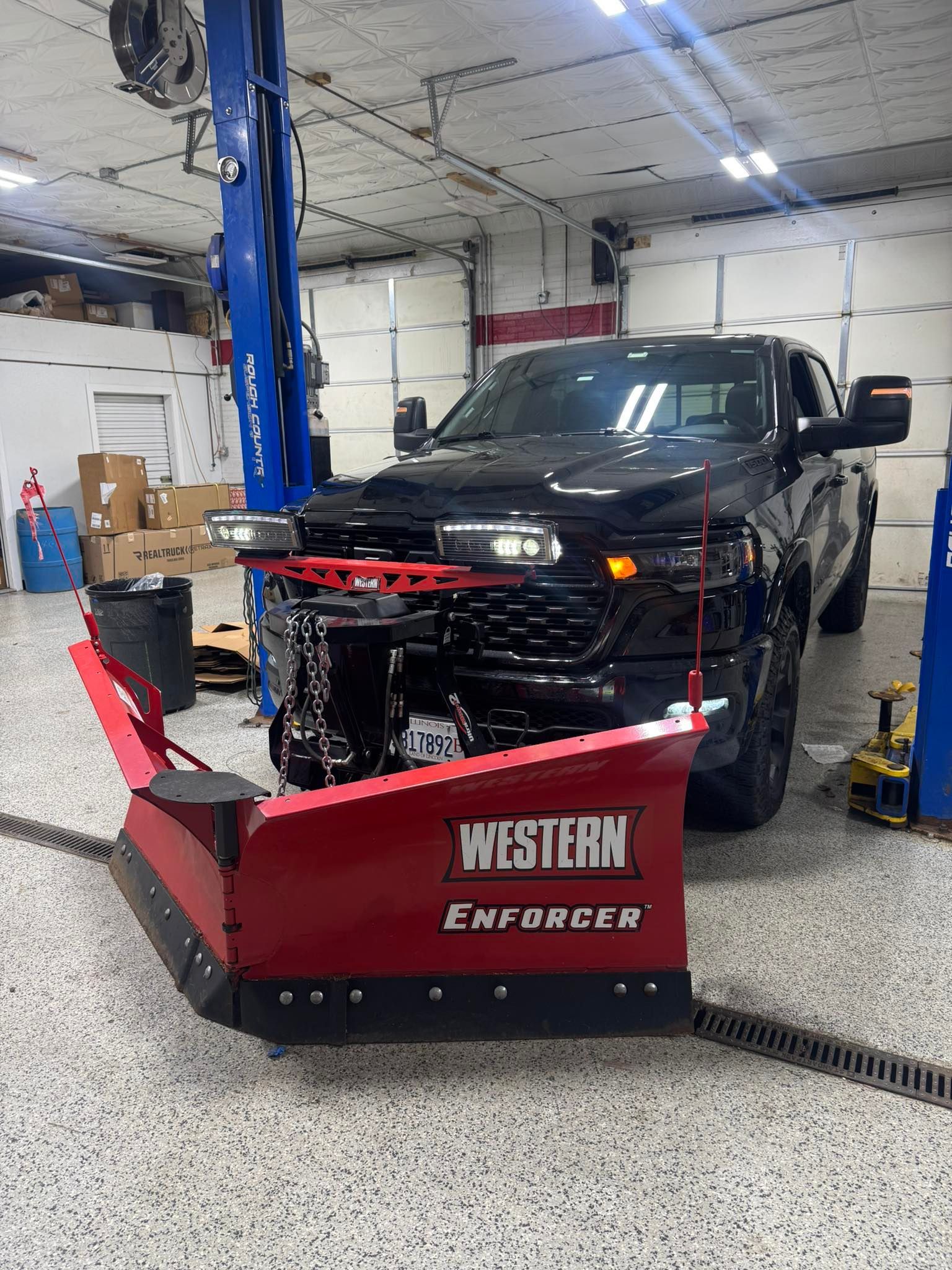Black pickup truck with a red Western Enforcer snow plow in a garage