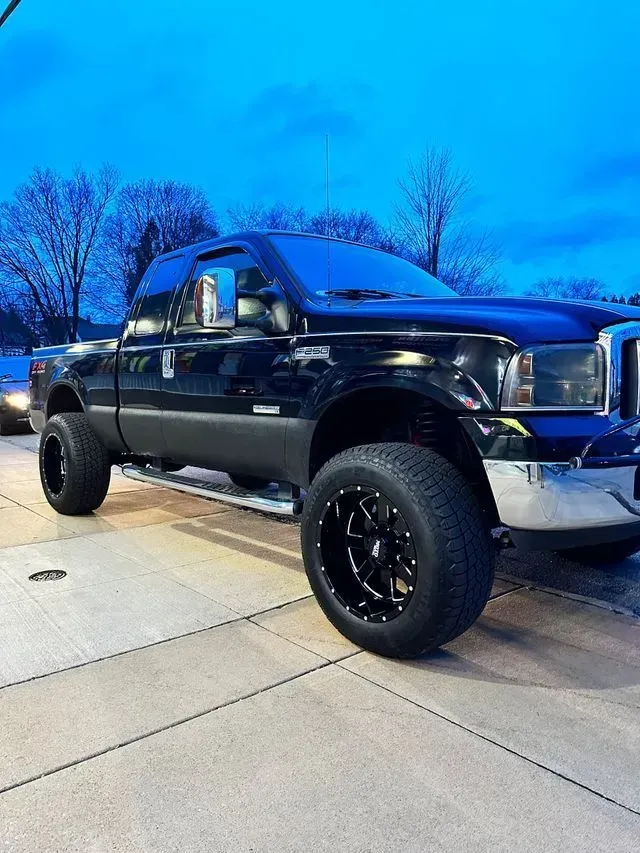 Black lifted pickup truck parked on a driveway at dusk, with blue-tinted sky in the background