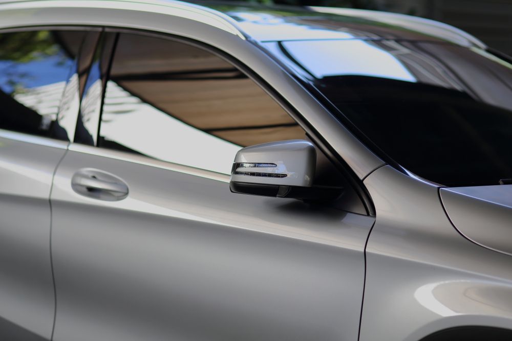 Silver car side view with tinted windows and side mirror, parked outdoors