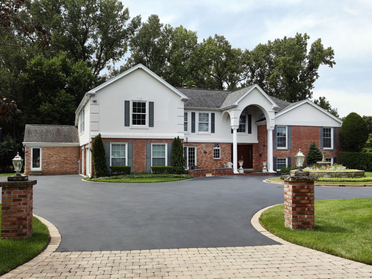 A large white and brick house with a black driveway