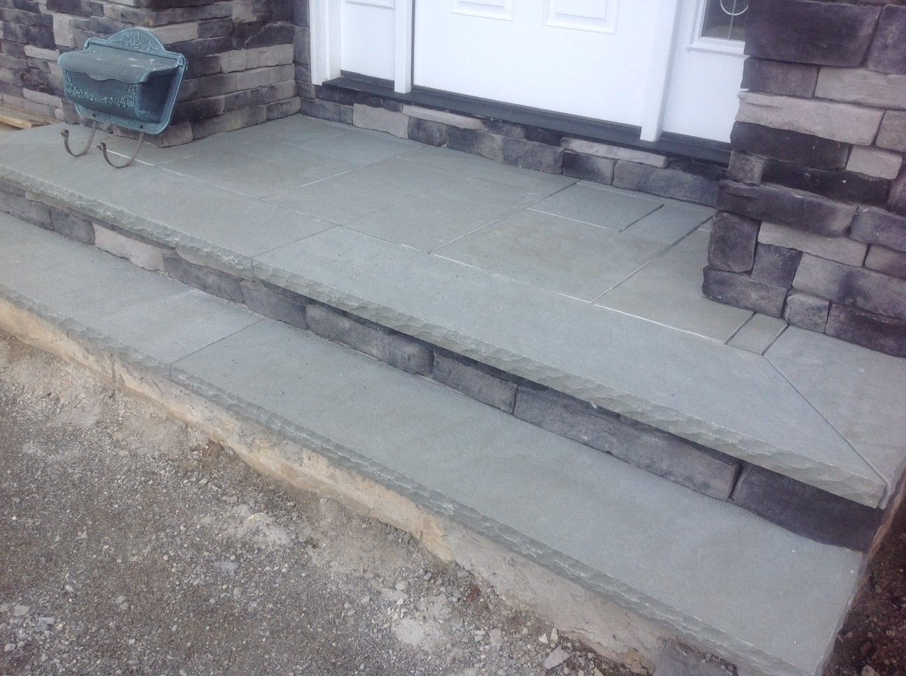 A set of steps leading up to a door with a wheelbarrow in the background.