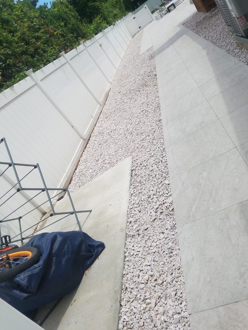 A concrete walkway with gravel and a white fence