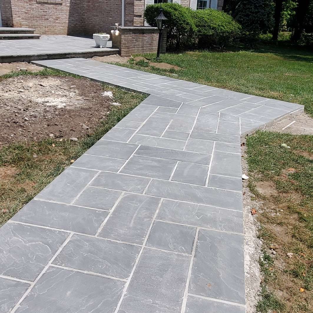 A brick walkway leading to a house in a yard