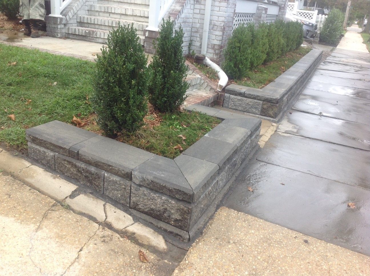 A stone wall with a planter in the middle of it next to a sidewalk.