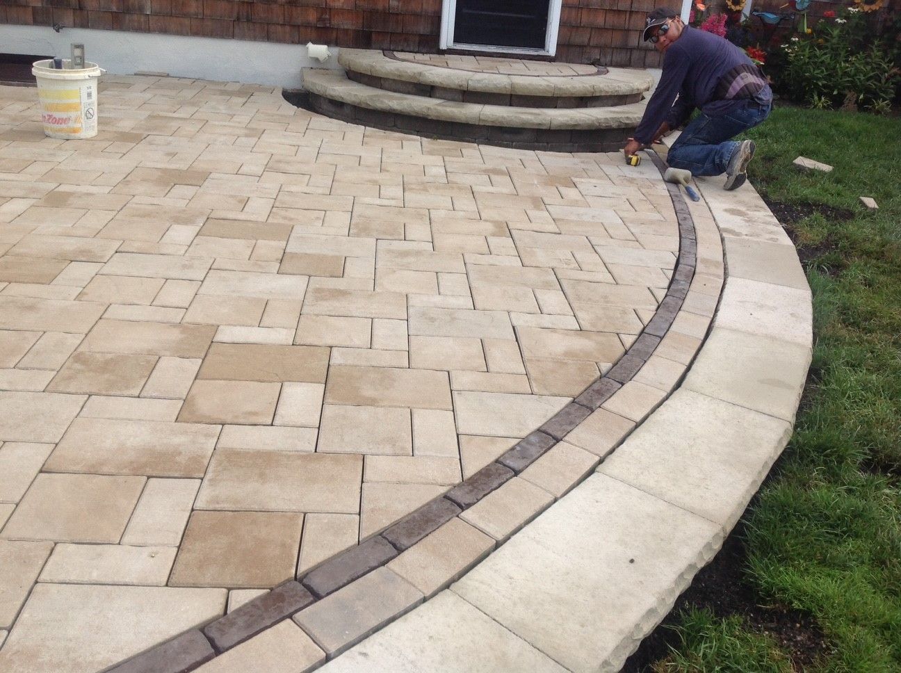 A man is kneeling on a brick walkway in front of a house