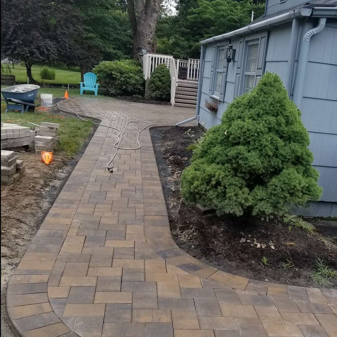 A brick walkway leading to a house with a blue chair in the background