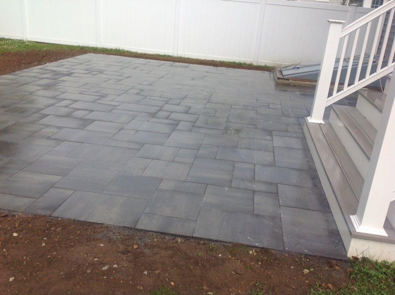 A patio with a white railing and stairs next to a white fence.