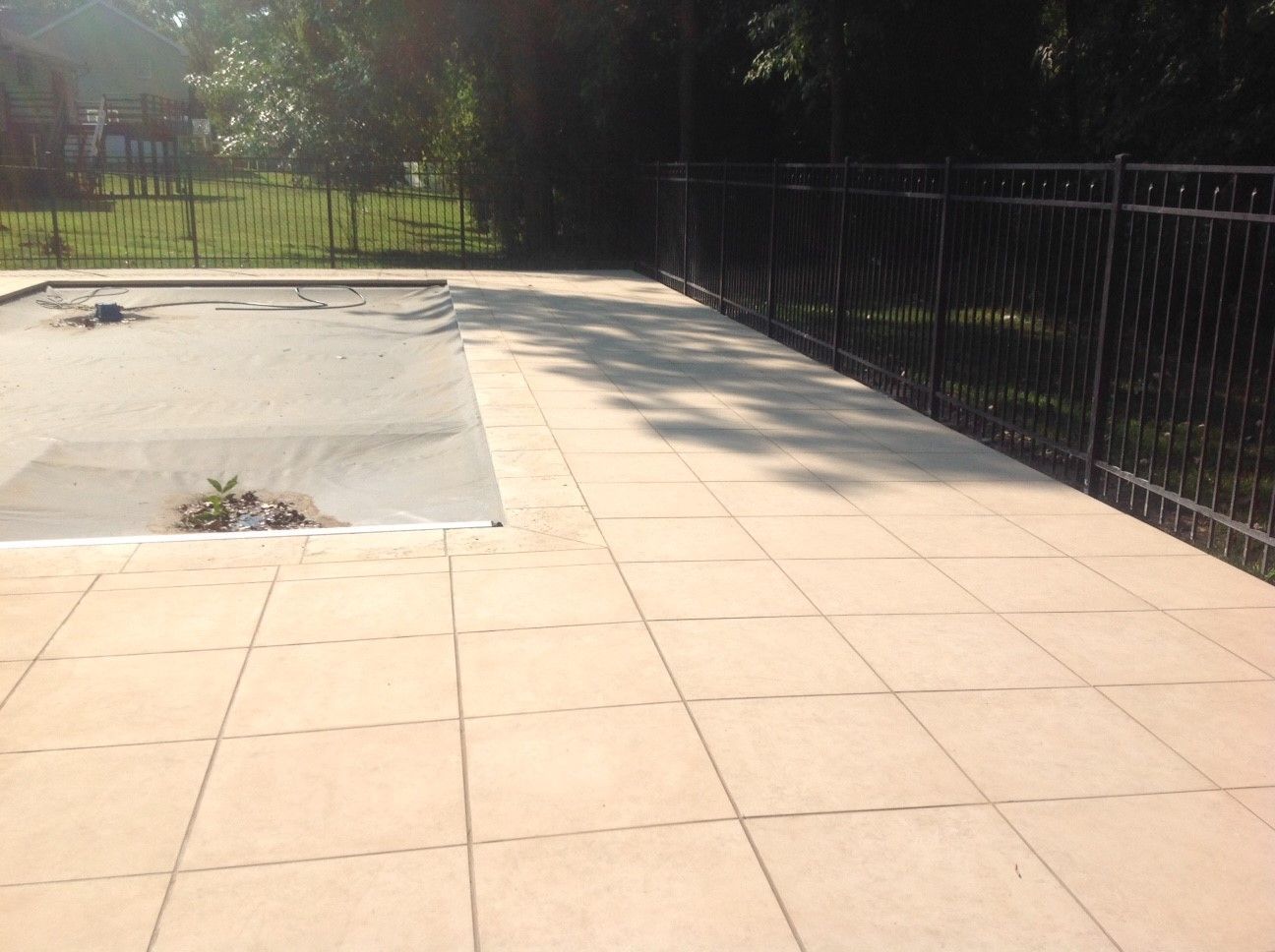 A fence surrounds a swimming pool with a patio in front of it.