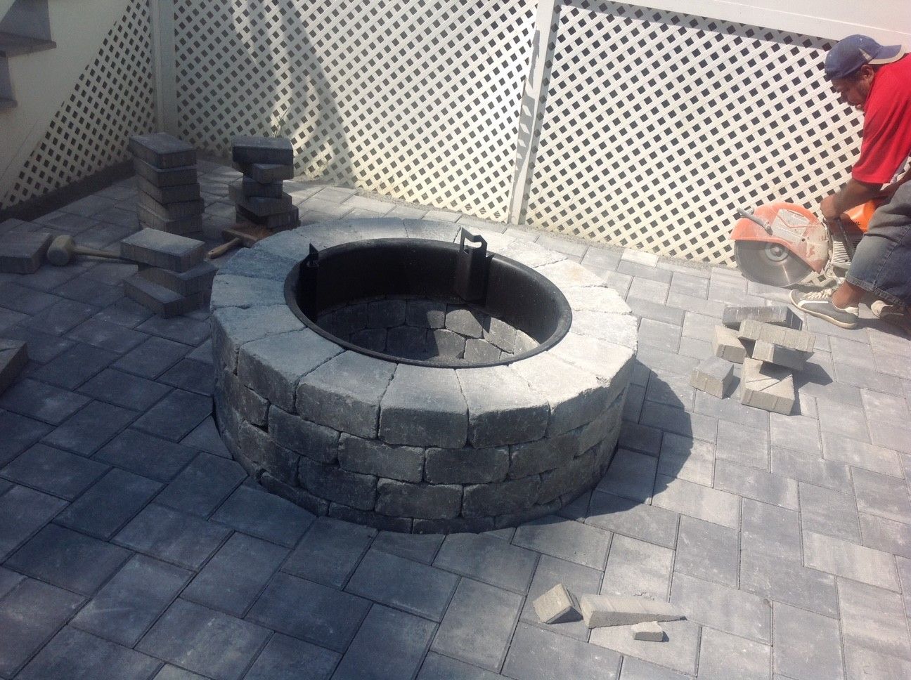 A man is laying bricks around a fire pit on a patio.