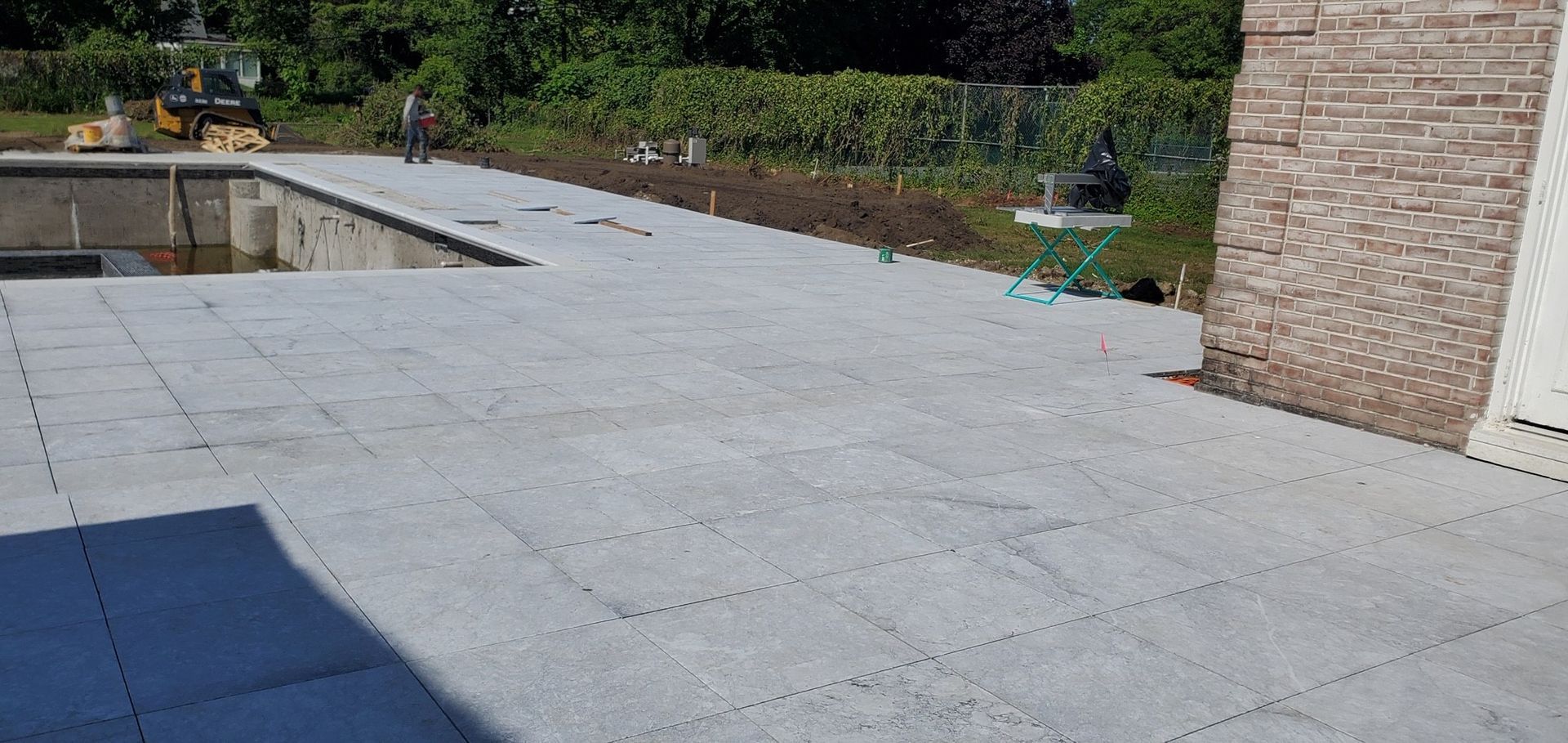 A patio with a pool in the background and a brick building in the background.