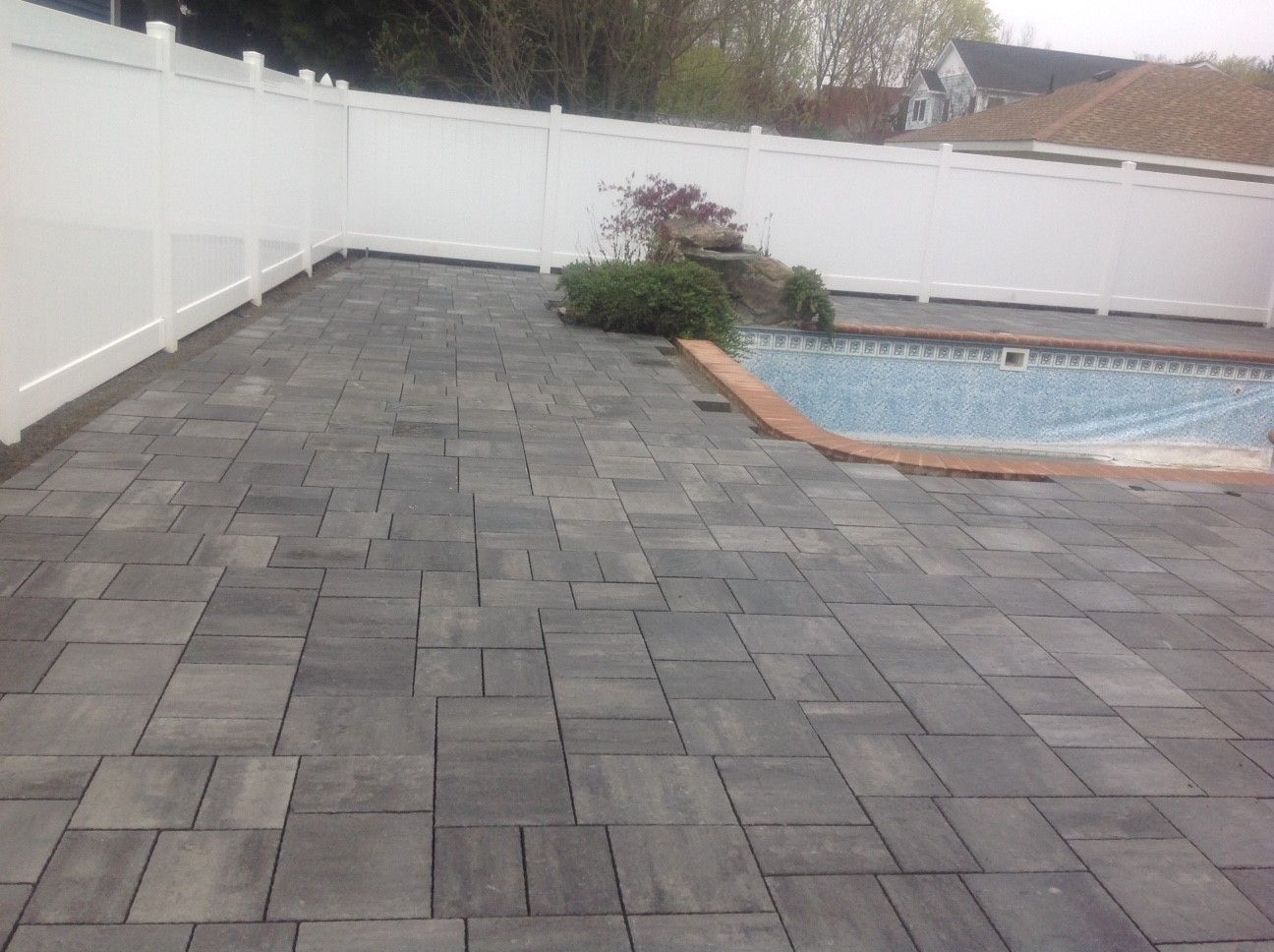 A patio with a pool and a white fence in the background.