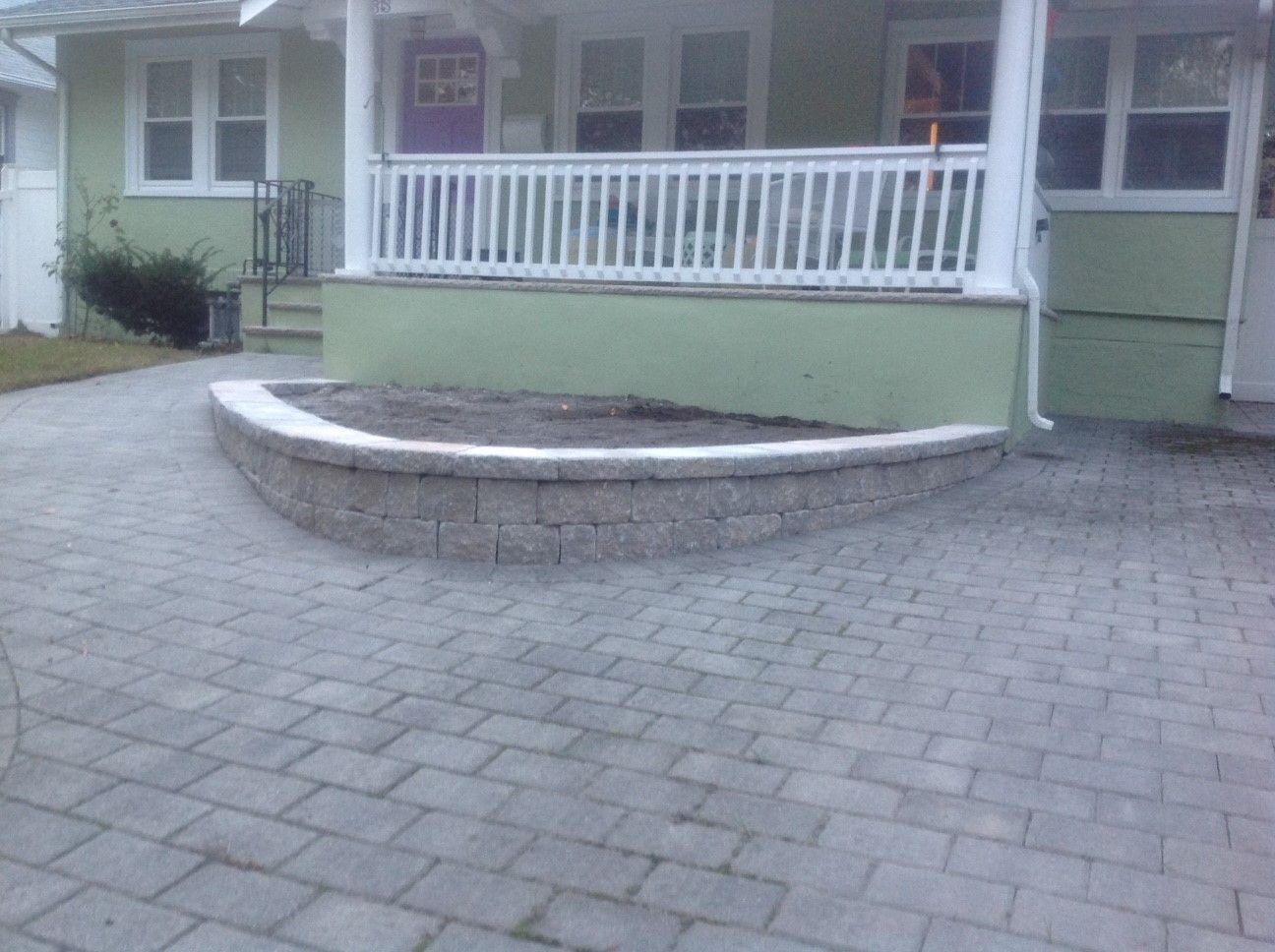 A brick walkway leading to a green house with a white porch.