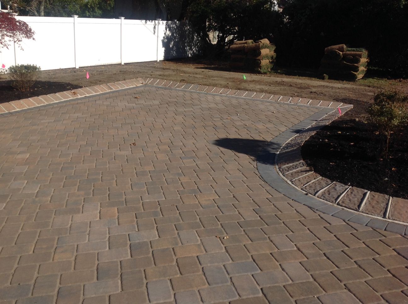 A brick driveway with a white fence in the background